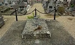 Une tombe plutôt discrète sur laquelle sont posés un crucifix et une plaque.