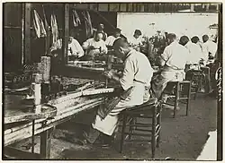 Photographie montrant des ouvriers travaillant dans une sardinerie bretonne (photographie par Paul Géniaux, conservée au Musée de Bretagne à Rennes).
