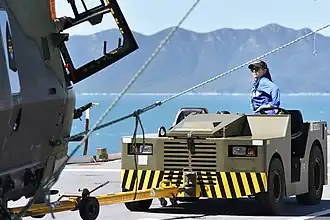 Remorqueur EINSA sur le pont du porte-aéronef HMAS Canberra tractant un hélicoptère.