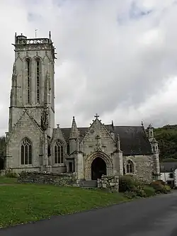 Photographie d'une église avec, de gauche à droite, la tour surmontant une chapelle, une lucarne, un porche sculpté, puis le chevet