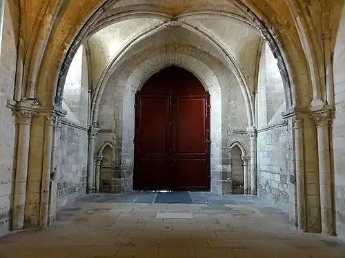 Même porte rouge vue de l'intérieur, dans une pièce vide surmontée d'une croisée d'ogives.