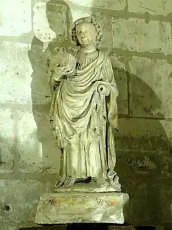 Statuette de marbre blanc représentant un homme souriant tenant une boîte de la main gauche« Statuette : saint Quentin », sur Inventaire général du patrimoine culturel des Hauts-de-France, 2010..