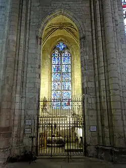 Haute pièce surmontée d'une croisée d'ogives et fermée une grille en fer forgée. Une verrière bleutée représentant une quinzaine de personnages donne dans vers l'extérieur.