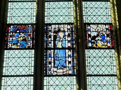 Le vitrail central représente saint Quentin dans un édicule gothique. Le vitrail de gauche, plus petit, présente l'intérieur de la maison d'un drapier. Le tailleur est en train de couper une pièce d'étoffe rouge tandis que sa femme, assise à ses côtés, travaille sur une pièce d'étoffe bleue. Sur le vitrail de droite, de même taille que le précédent, deux portefaix déchargent leur fardeau devant un bâtiment, que l'historien Georges Lecocq suppose être l'ancienne halle au blé de Saint-Quentin.