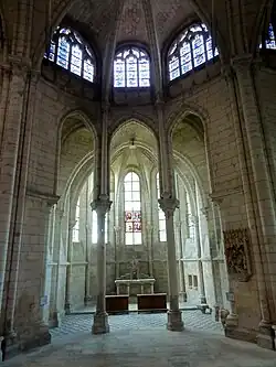 Chapelle contenant du mobilier en bois et un groupe sculpté accroché au mur de droite, surmontée de trois vitraux décoratifs.