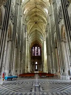 Grand espace sous des voûtes soutenues par des piliers. Au fond en haut de l'image, de grandes verrières sont visibles.
