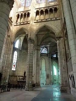 Grande arcade de pierre donnant accès au déambulatoire. Des tirants de bois soutiennent les voûtes. A gauche de l'arcade, un autel est aménagé et supporte une statue en bois.