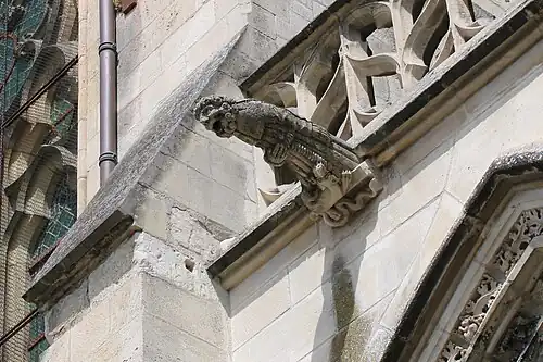 Gargouille représentant un moine barbu semblant terrifié. À ses pieds, un dragon menaçant.