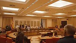 Une salle de réunion avec des fauteuils, des bureaux et des personnes.