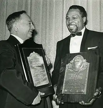 Deux hommes souriants en costumes de cérémonie portent des récompenses de la cérémonie de Boxer de l'année de 1959. A gauche, Sam Taub regarde Archie Moore.