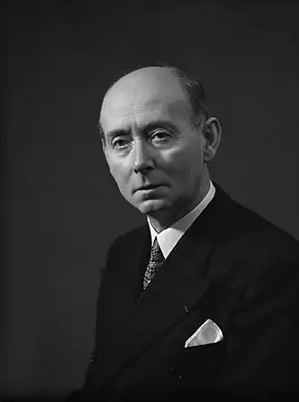 Photographie noir et blanc d'un homme chauve, de face.