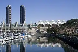 Photographie en couleurs représentant un bâtiment moderne en tubulures blanches au premier plan, et deux tours à l'arrière-plan.