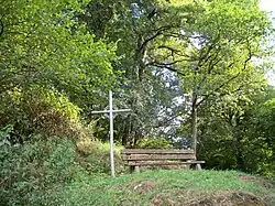 Une croix en fer forgé et un banc placé sur le chemin