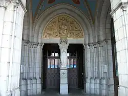 Le porche et l'entrée. Sur le pilier central est placée une statue de Notre-Dame de Lourdes. Sur le tympan du portail sont représentés le Christ pantocrator et le tétramorphe