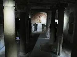 Photographie en couleurs d'une pièce sombre dont le plafond est supporté par des colonnes.