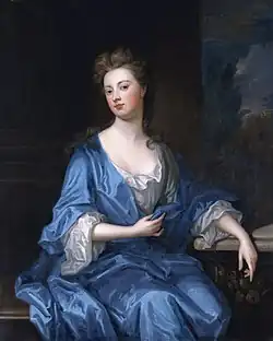 Portrait en pied d'une femme assise portant une robe bleue.