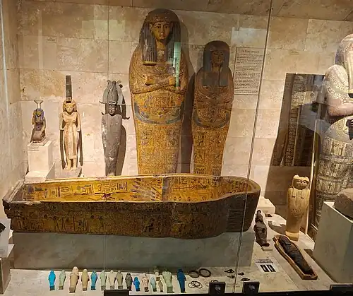 Sarcophages. Bois stuqué polychrome. Au sol sarcophage au nom de Khonsou-Mès de la XXIIe dynastie : Troisième période intermédiaire. Petits Ouchebtis colorés (serviteurs du mort dans l'au-delà) et Œil oudjat (œil, protecteur, d'Horus).