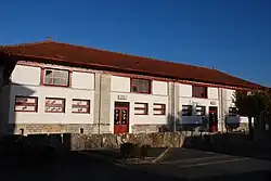 Photographie d’un édifice allongé en quatre parties égales, aux boiseries rouge et à un seul étage.