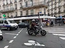 Un deux-roues motorisé arrêté après la ligne d'effet du feu tricolore, sur un sas vélo.