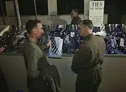 En 1944, dans un centre de démobilisation au Royaume-Uni, un militaire (à gauche), pour choisir une cravate qui puisse s'accorder avec la chemise de sa future tenue civile, est conseillé par un membre des Royal Army Ordnance Corps (en) (à droite).