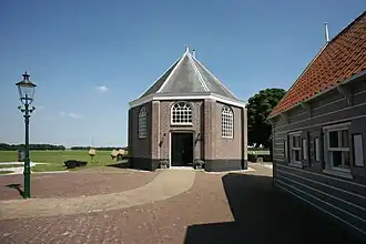 Photographie en couleurs d'un bâtiment précédé par une maison au premier-plan