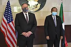 Deux hommes en costume et cravate debout de face avec leurs drapeaux en arrière-plan