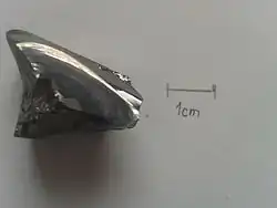 Photographie rapprochée d'un cristal de sélénium sur fond blanc, à proximité d'une échelle pour mesure.