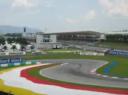 Piste goudronée de Formule 1 au niveau d'une chicane, avec une tribune en arrière plan
