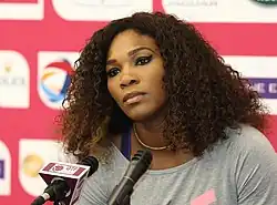 Portrait photographique en couleurs de Serena Williams, l'air sérieux, devant un micro de presse.