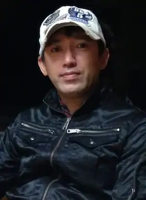 Photo en couleur d'un homme asiatique portant un blouson noir et une casquette blanche.