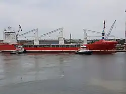 Un vraquier à quai flanqué de deux remorqueurs.