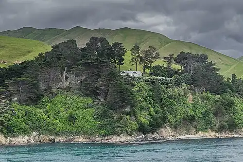 Photographie d'une maison située sur une falaise et entourée d'un petit bois.