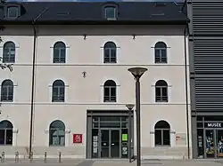 Photographie en couleurs et de face de la façade d'un bâtiment gris et beige.