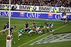 Ligne de joueurs en vert à droite, en défense, proche de sa ligne, défendant face à des adversaires en bleu.