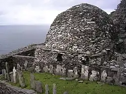 Photographie en couleurs d'un bâtiment en forme de dôme et appareillé de pierres grises et blanches, un cimetière venant le longer au premier plan.