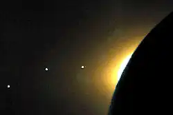 Image sombre où l'on devine la Lune à droite devant le Soleil. Trois points blancs sont alignés à gauche.