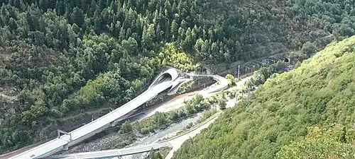 Photographie d'une sortie de tunnel desservant plusieurs axes routiers, le tout étant entouré de forêts denses et vertes.