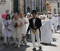 Un homme à lunettes, habillé d'un haut-de-forme et d'une queue-de-pie, dirige un cortège de Soufflaculs, tous vêtus de chemises de nuit blanches et de bonnets de coton blanc, avec à leurs mains des soufflets.