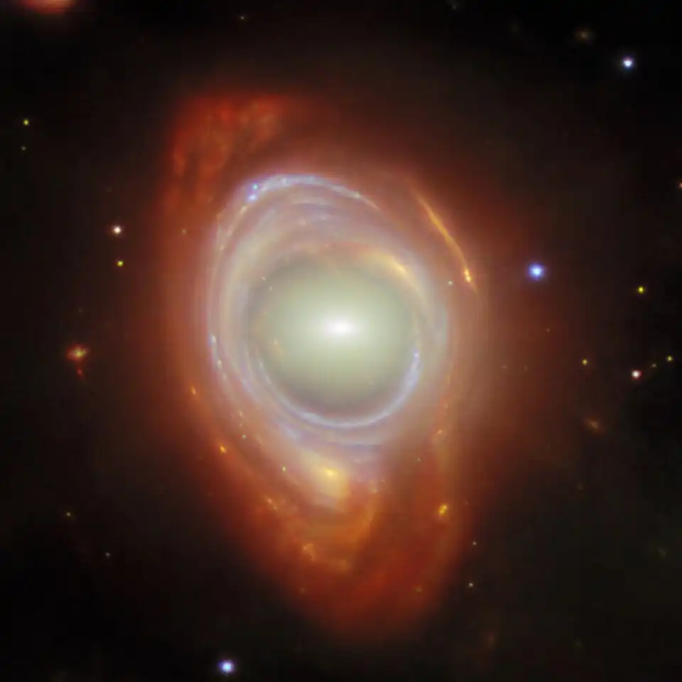 Une galaxie spirale déformée par une galaxie elliptique plus proche (potm2503a), les deux étant parfaitement alignées. Photo de 2025 issue des télescopes spatiaux James Webb et Hubble.