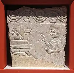 Figure d'un personnage de profil présentant une offrande, une tête de bétail, sur une table