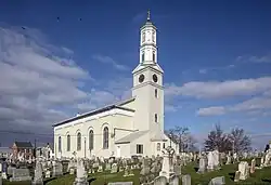 L'église catholique Saint-Joseph. Le clocher surplombe le bâtiment de style Greek Revival, italianisant et fédéral. Au premier plan, des tombes entourent l'édifice.