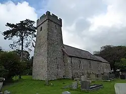 Photo d'un bâtiment allongé aux murs de pierre grise, flanqué d'une grande tour carrée au premier plan à gauche