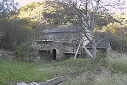 Ancienne église aperçue derrière un arbre qui a perdu ses feuilles pour l'hiver. Sur la façade, un échafaudage artisanal.