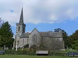 Photo d'un bâtiment en pierre grise flanqué d'une tour à la flèche élancée