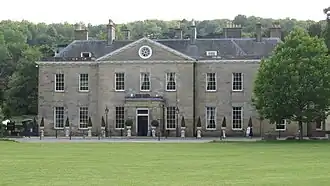 Photo d'un manoir à deux étages aux murs gris avec de nombreuses fenêtres, situé au milieu d'une pelouse verte