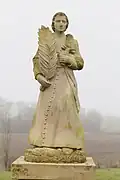 Statue montrant un homme en soutane, tenant dans sa main droite une palme et une croix dans la main gauche.