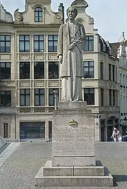 statue en pierre de Massangis (gris pâle) représentant la reine debout sur un socle au milieu d'une petite place