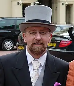 Homme en costume, barbu, avec des lunettes et portant un chapeau blanc
