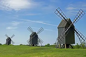 Trois moulins à vent quasi-identiques en bois alignés dans un paysage ouvert.