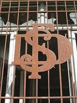 Sigle S.D.F. (Sucrerie et Distillerie de Francières) en métal forgé sur des barreaux de fenêtres de bureau. Les lettres S, D et F sont entrelacées.